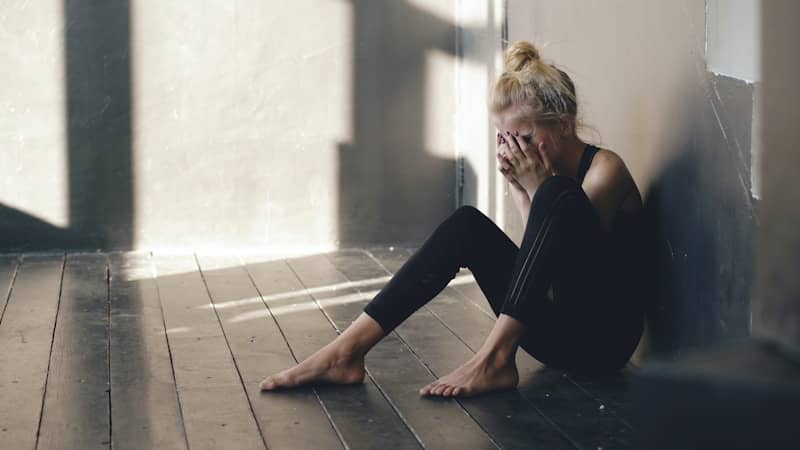 Woman sitting on floor, covering face with hands.