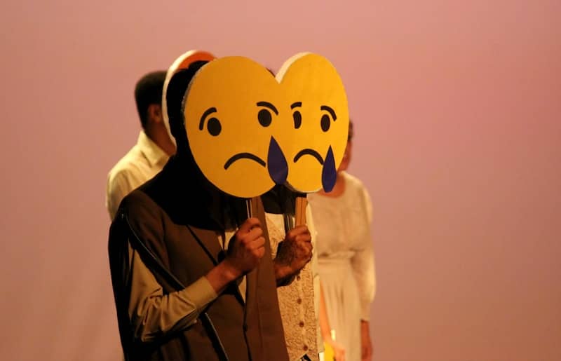 a woman holding a cardboard heart with a sad face on it
