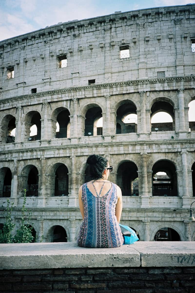 A woman sitting on a ledge in front of an ancient building