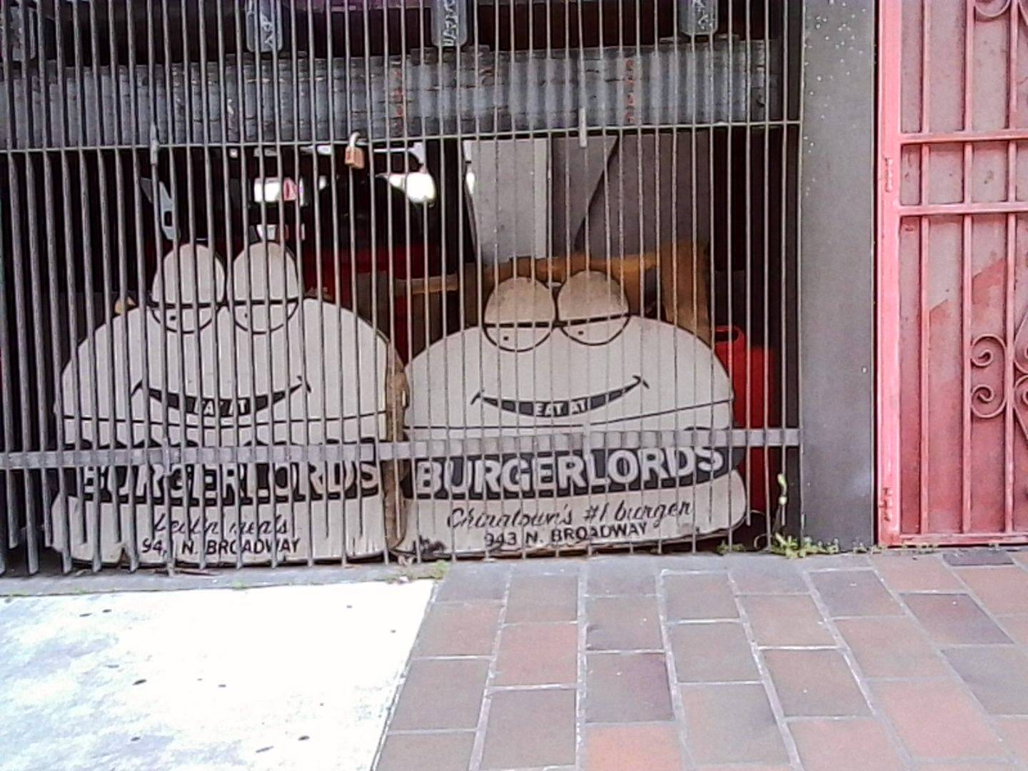 two signs of hamburgers with sleepy eyes reading BURGERLORDS behind a gate