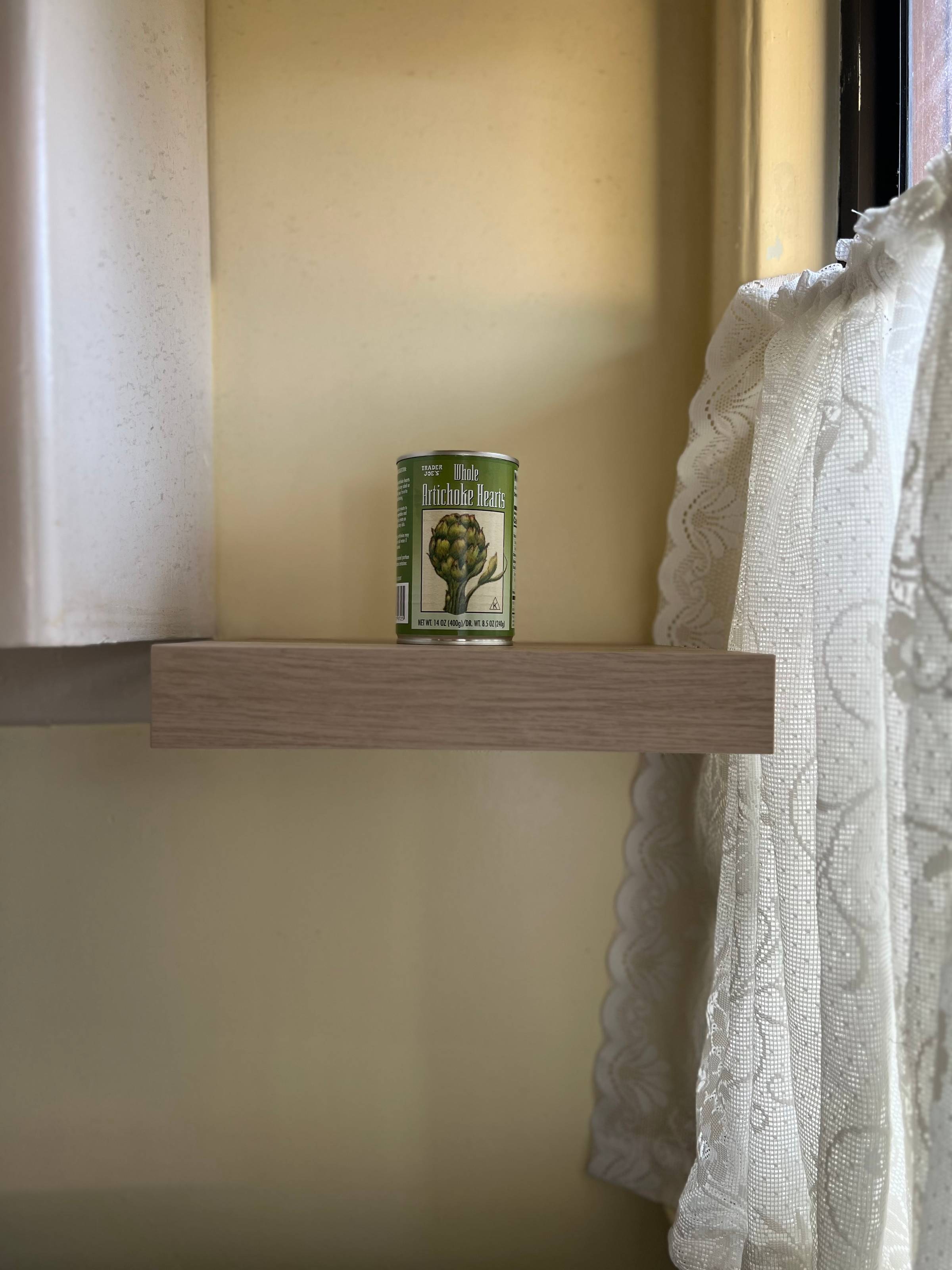 a can of artichoke hearts on a shelf next to a window
