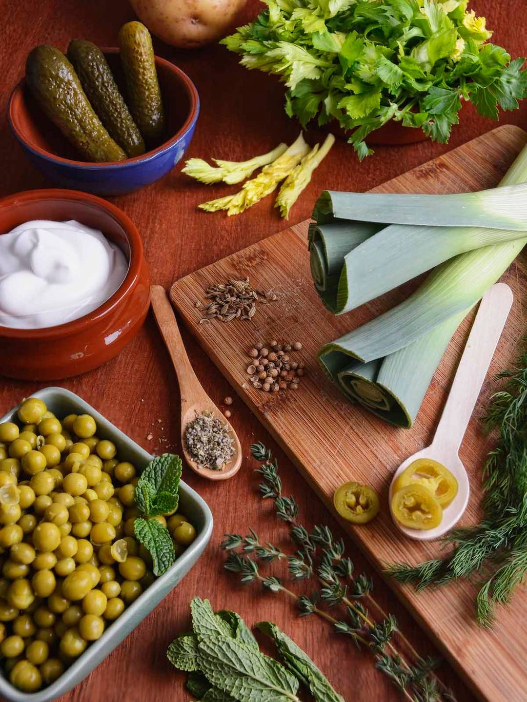 Fresh and dried ingredients for pea and pickle soup laid out on rustic wooden board, terracotta bowls and wooden spoons.