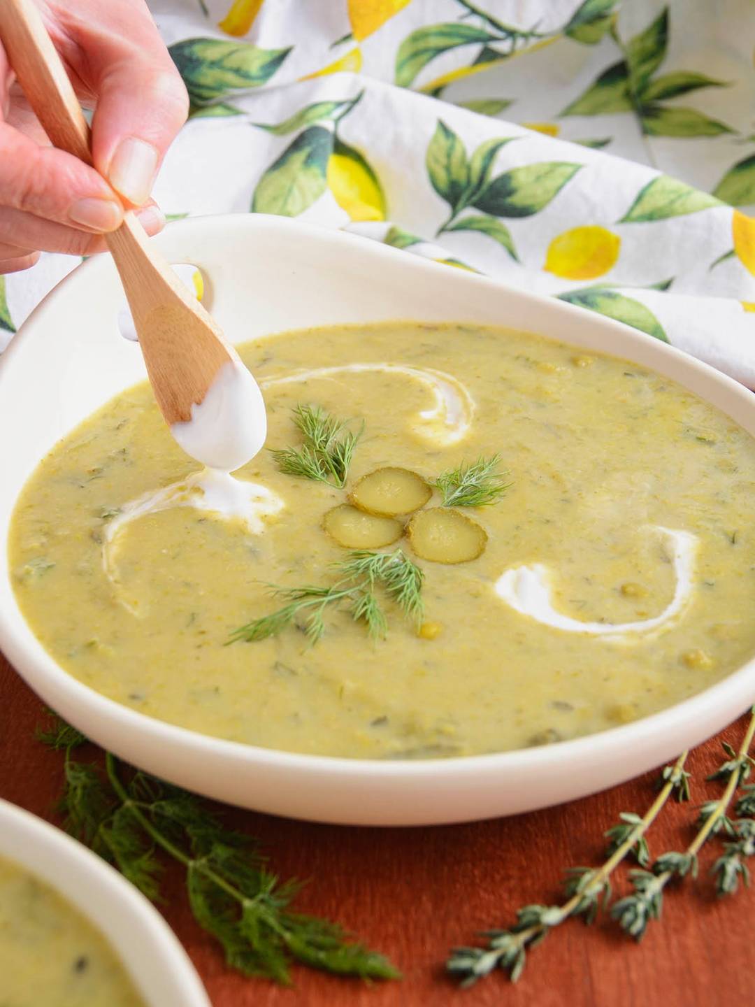 Adding swirls of coconut yoghurt as a finishing touch to a bowl of pale green pickle soup.