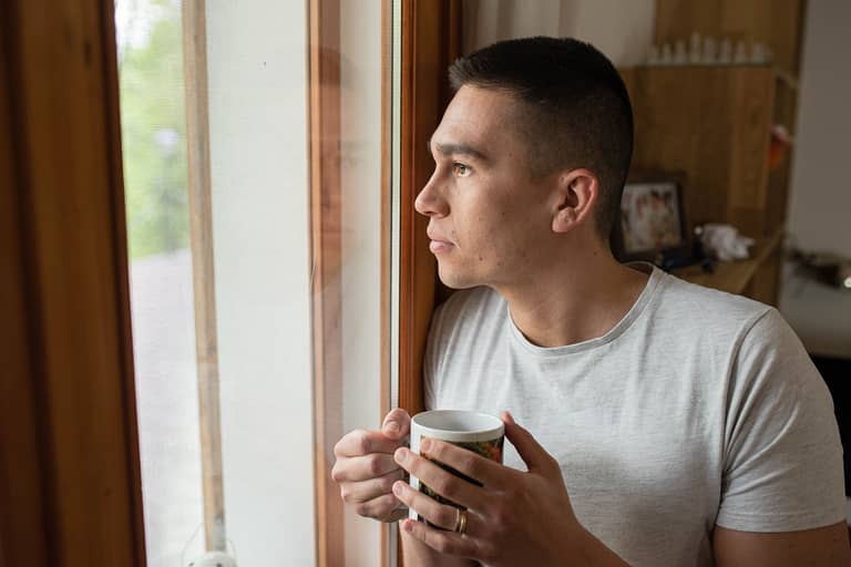 father looking out window reflecting on time, responsibility, and the life unfolding in the present