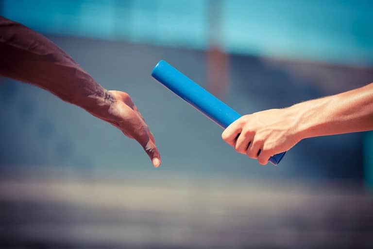 Two relay runners working together to complete a baton handoff