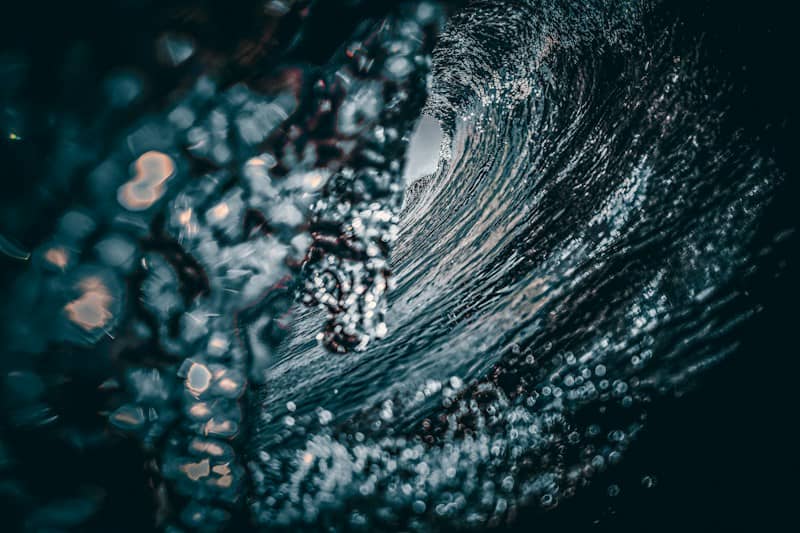 A dark ocean wave curling into a tube with bright bokeh light reflections