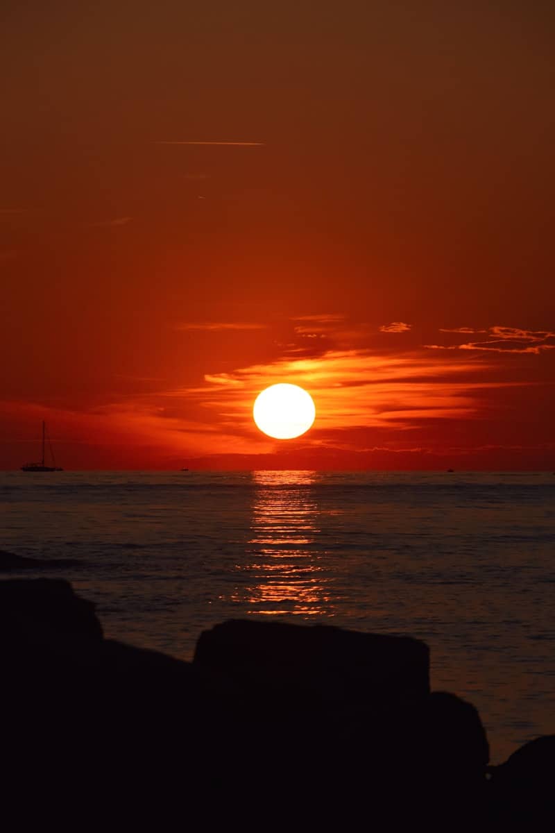 A sailboat on the horizon under a low sun and orange sky