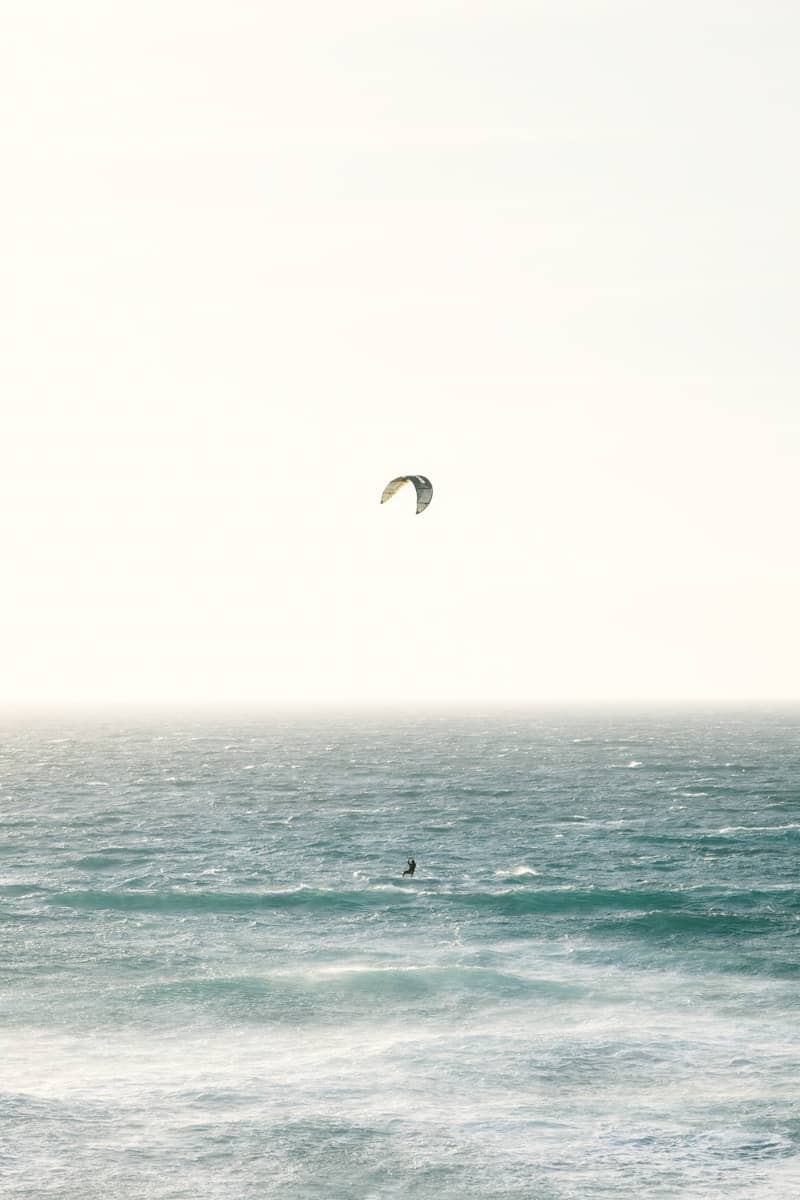 A person kitesurfing on the vast, hazy ocean.