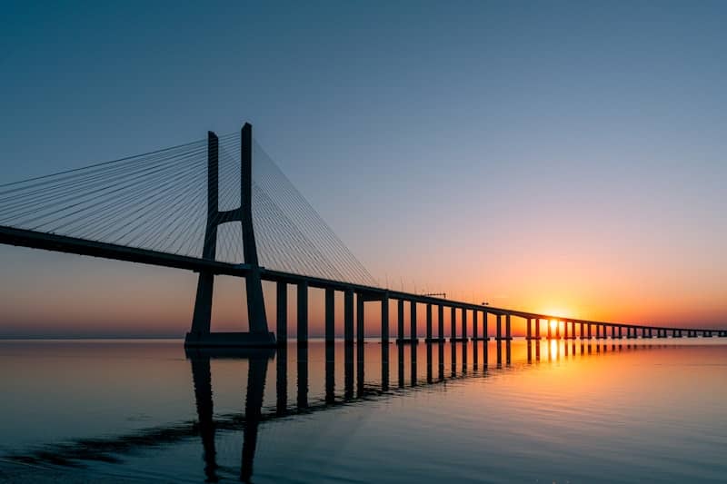 The sun is setting behind a bridge over water