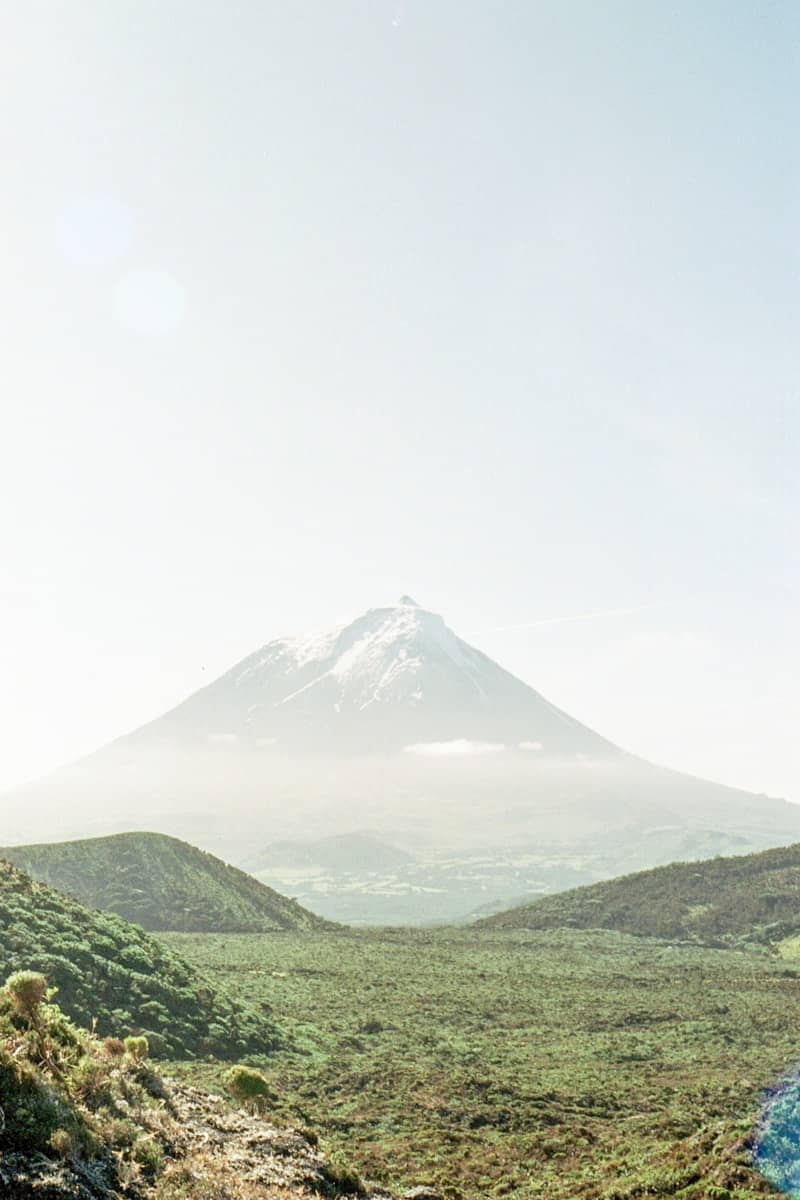 Snow-capped mountain rises above rolling green hills.