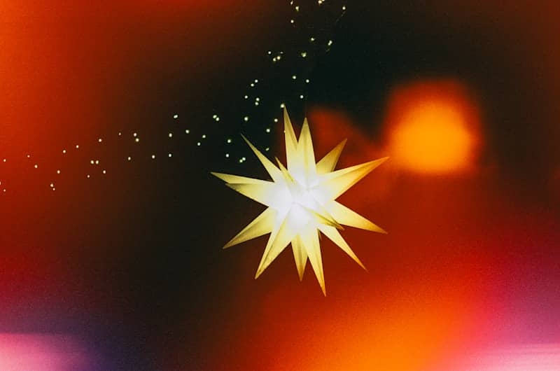 Abstract golden starburst with particles on a dark red background.