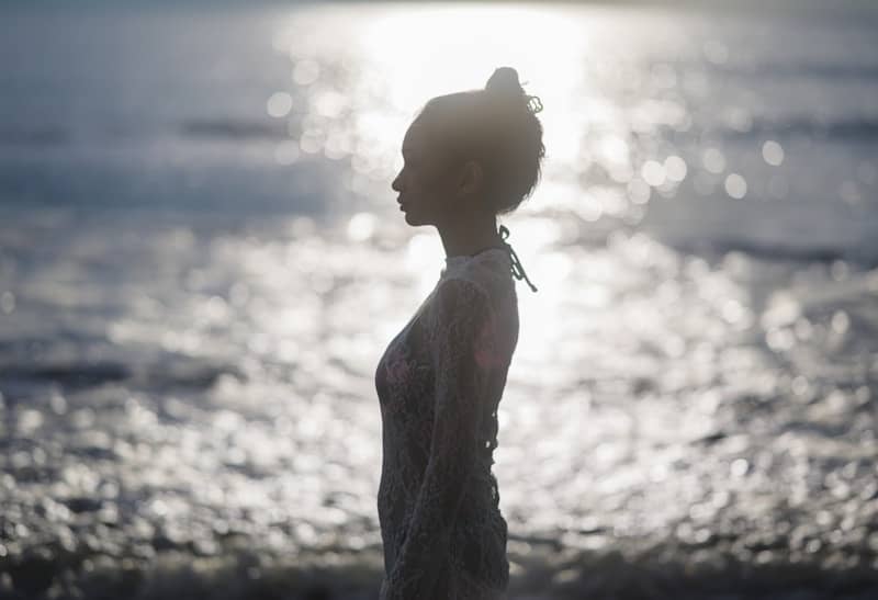 A woman in silhouette stands against the sparkling ocean