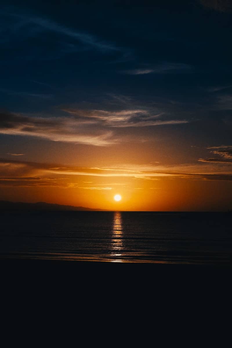 The sun is setting over the ocean on a cloudy day