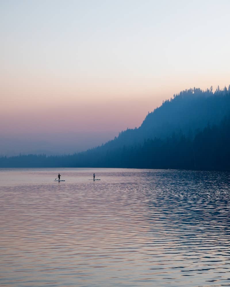 Paddleboarders enjoy a serene lake at dusk.