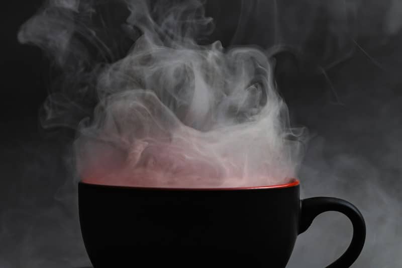 Thick white steam rising from a black mug with a red interior