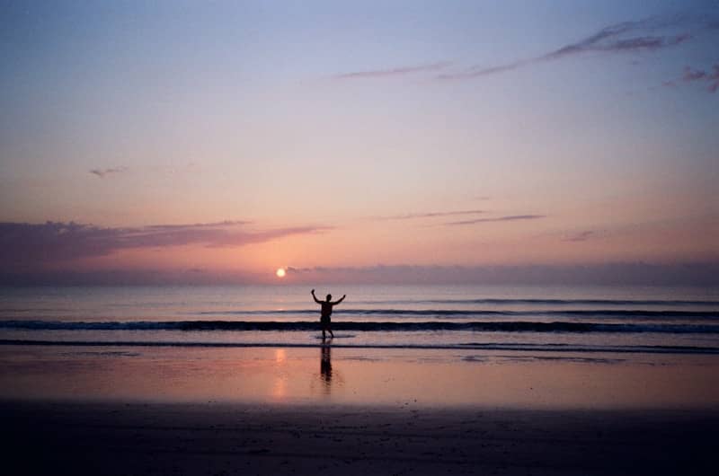 Person with arms raised at sunrise on a beach