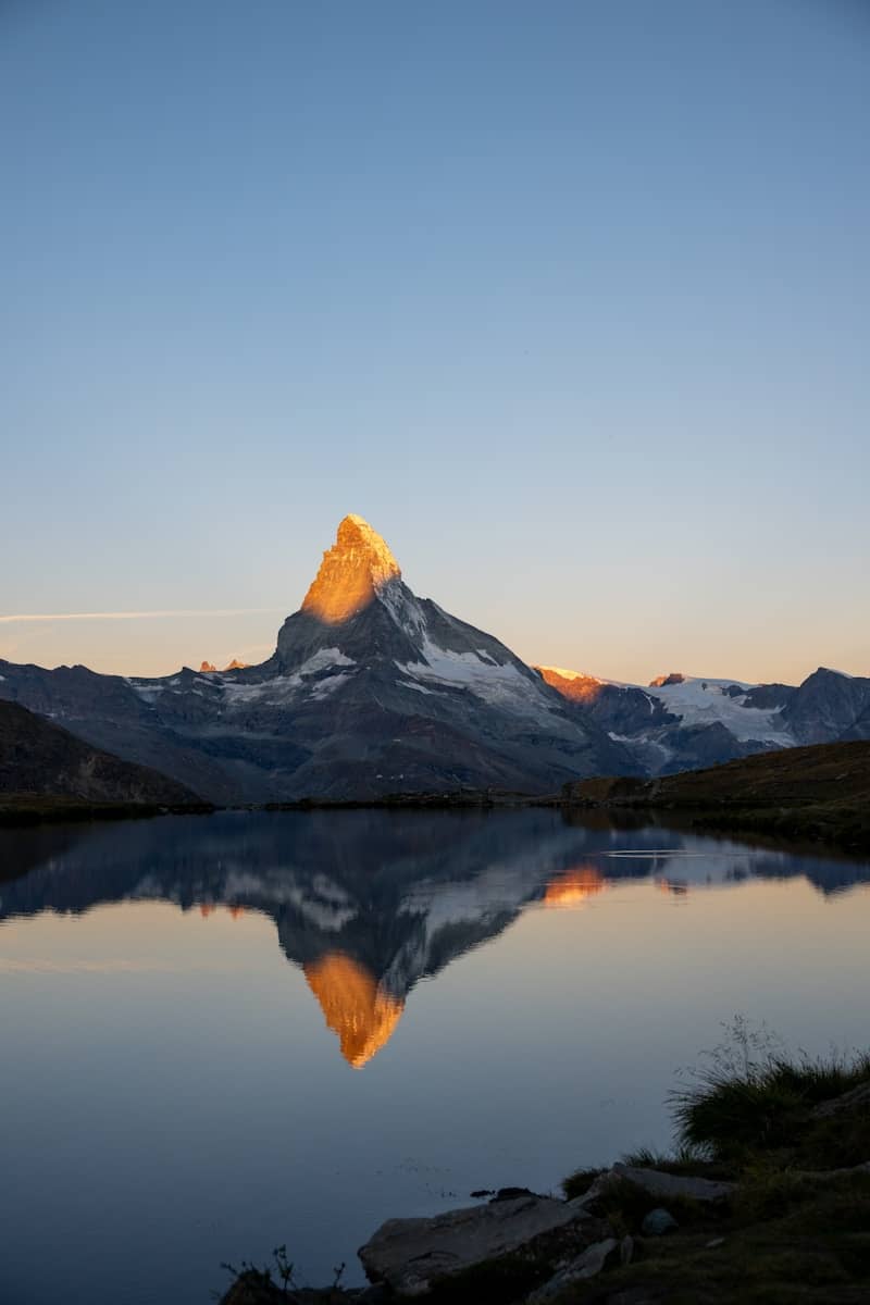 Mountain peak reflecting in calm lake at sunrise.