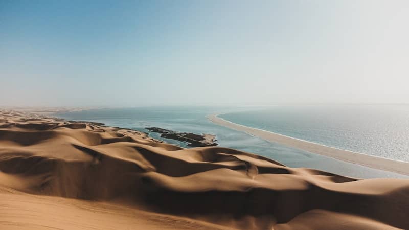 Sand dunes meet the ocean under a clear blue sky.