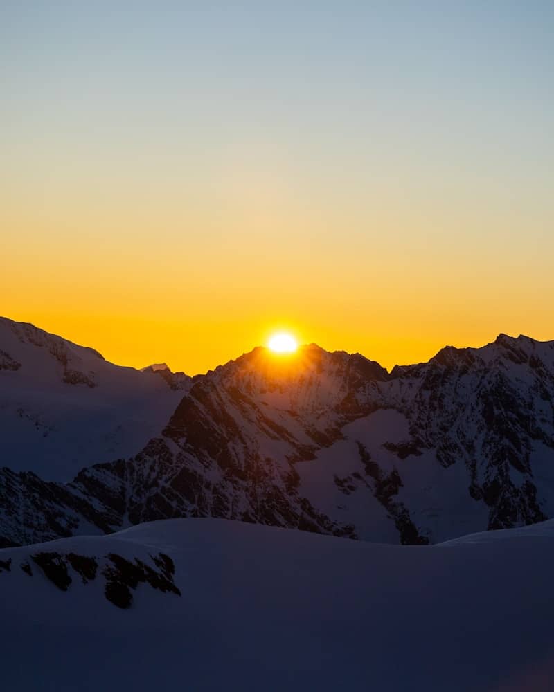 Sunrise over snow-capped mountains with clear sky.