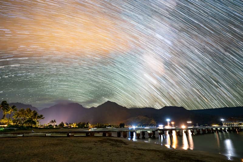 Long exposure star trails over a pier and mountains on a tropical coast