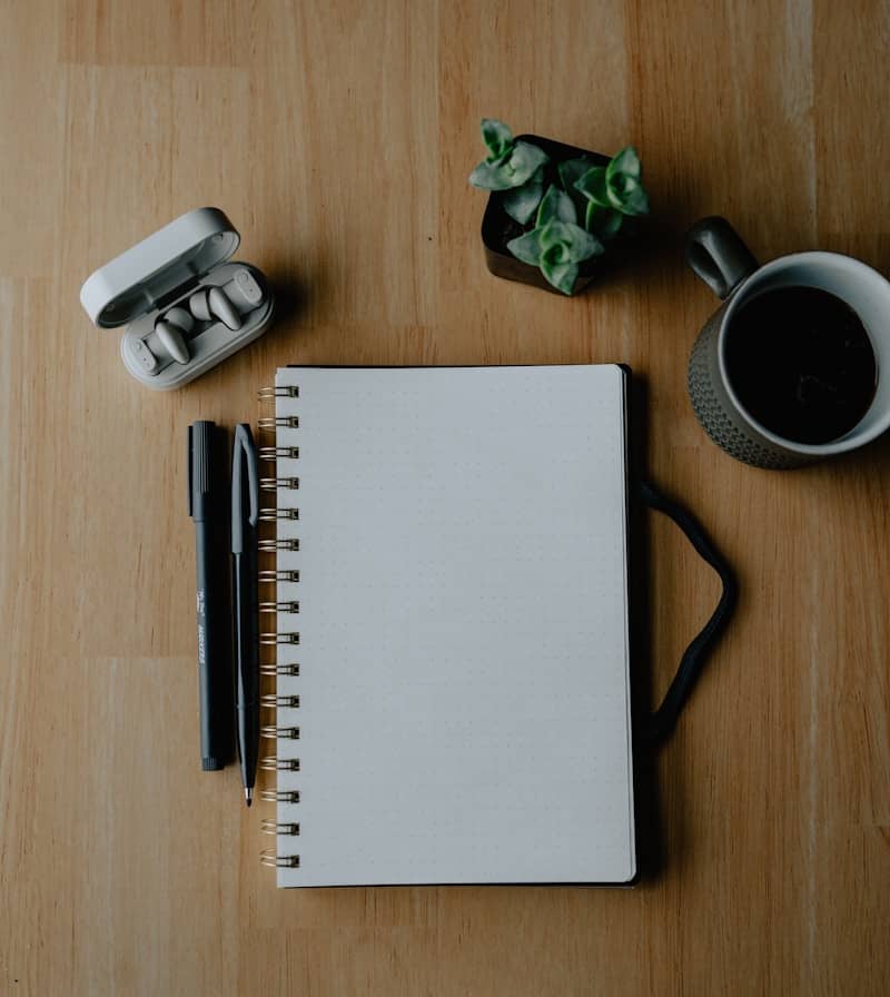 Notebook, pens, and coffee on a wooden table.