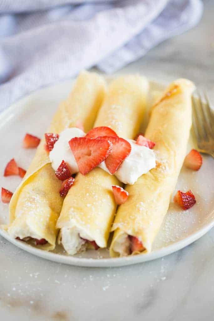 Strawberry crepes on a white plate garnished with cream and strawberries