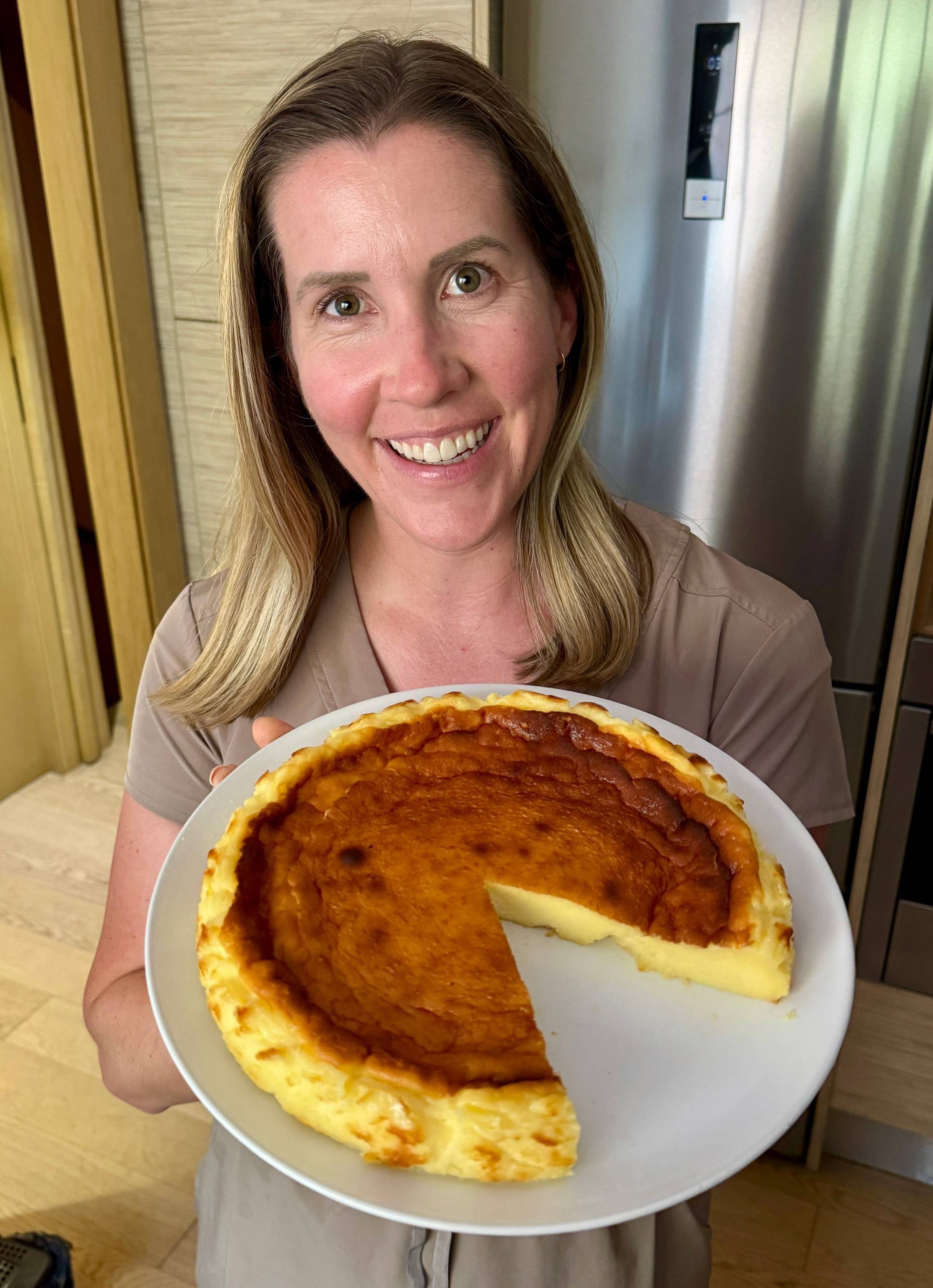 Lauren holding a new recipe for the Taste of Europe cookbook Basque Cheesecake! Cake has one slice out of it.
