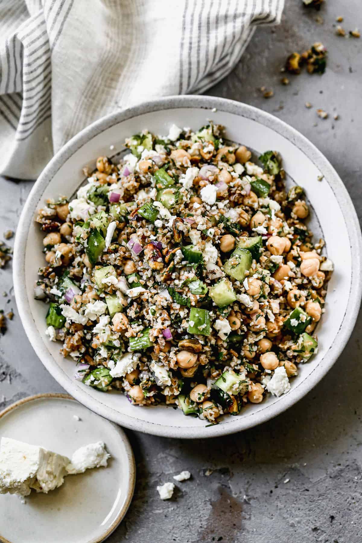 Bulgar Salad has crisp vegetables, feta cheese, and an easy dressing tossed with cooked bulgur.  Shown served in a large grey and white bowl.