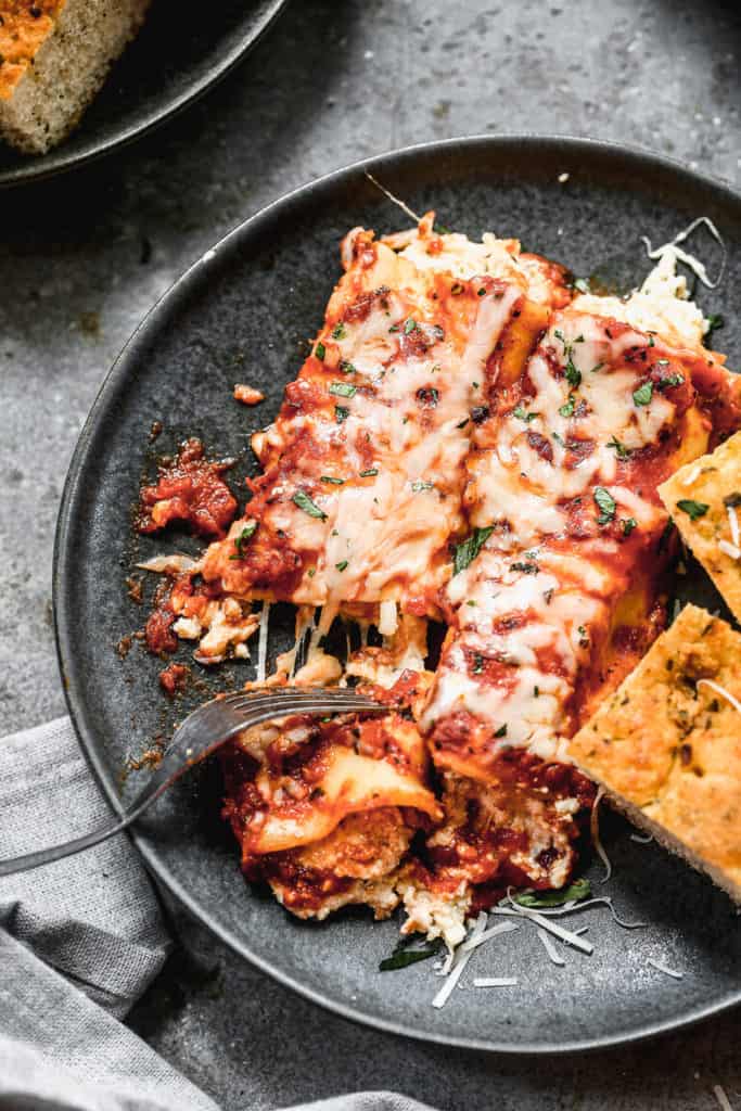 Manicotti served on a black plate and garnished with cheese and herbs