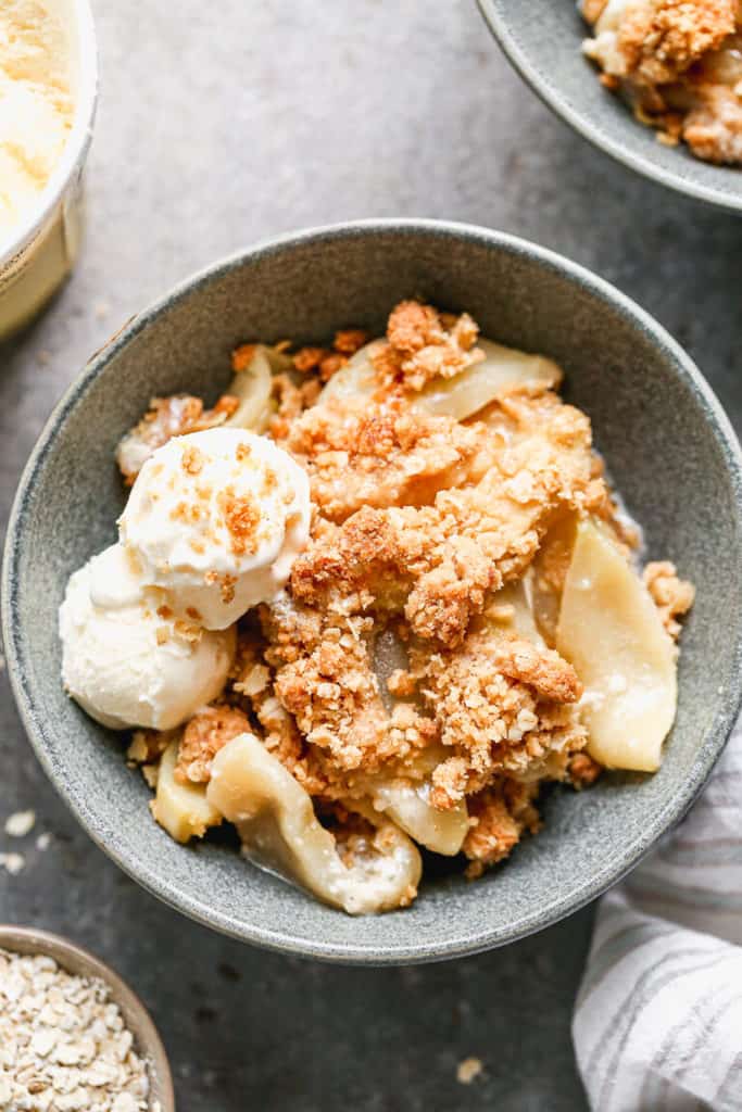 Apple crisp in a grey bowl topped with vanilla ice cream