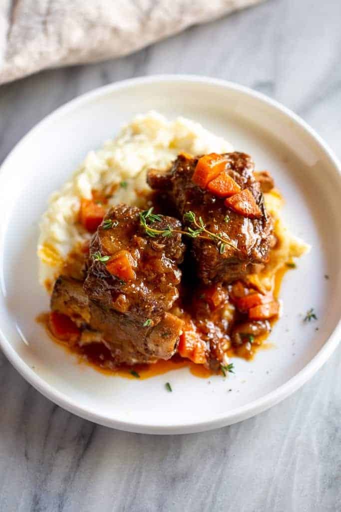 Braised Short Ribs served over mashed potatoes and topped with roasted vegetables and fresh herbs.