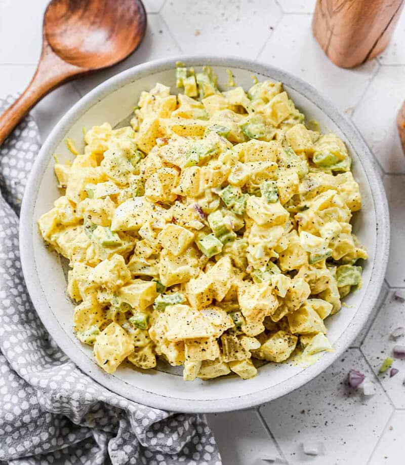 Classic Potato Salad served in a grey bowl surrounded by a kitchen towel and wood spoon.