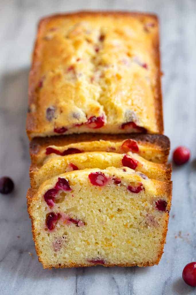 Cranberry Orange Bread sliced and garnished with fresh cranberries on a marble slab
