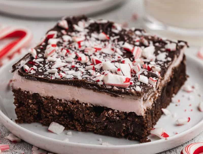 A square of homemade Peppermint Brownies on a white plate, topped with crushed candy canes.