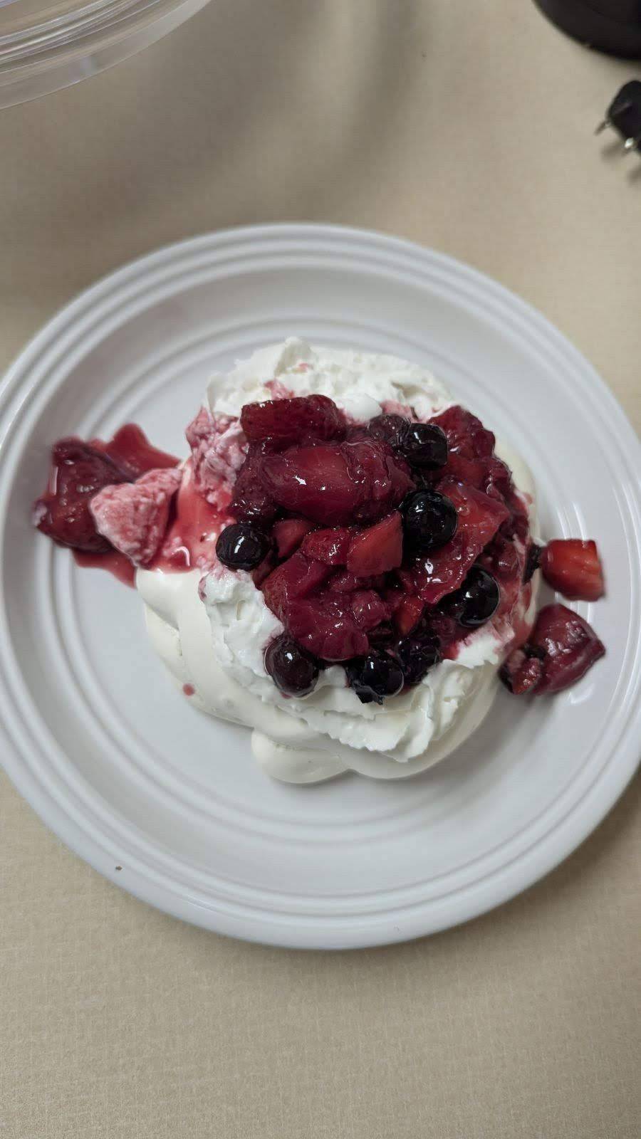 A delicate mini pavlova with a crisp meringue shell and soft, marshmallowy center, topped with whipped cream and fresh berries for a light and elegant dessert.