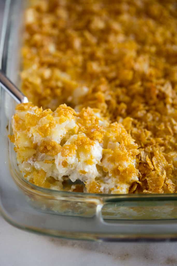 Funeral Potatoes being scooped out with a spoon from a glss 9x13 dish.