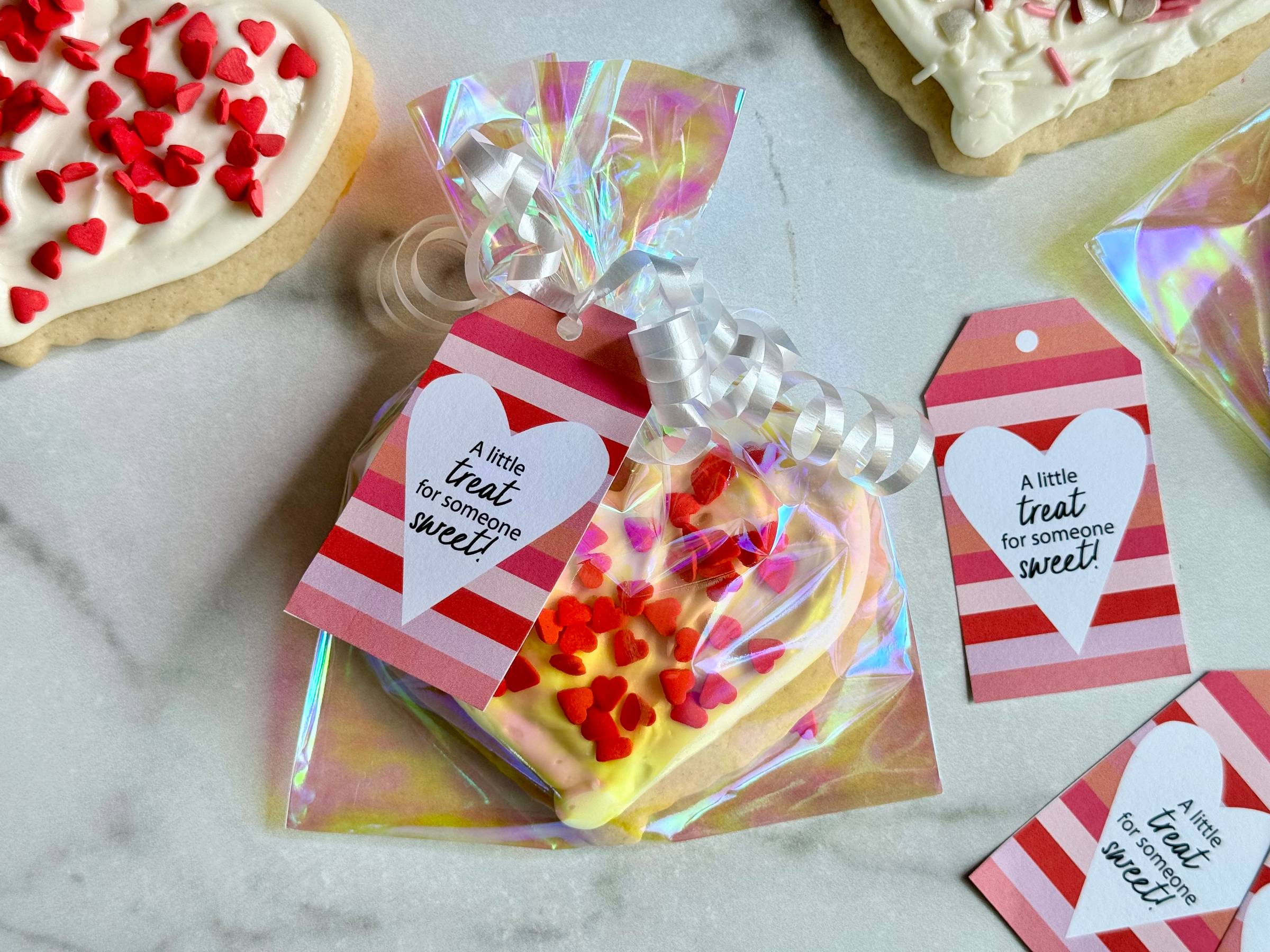 Gift idea of a Valentine's Sugar Cookie wrapped in clear plastic and tied with a ribbon. Tag says "A little treat for someone sweet!"