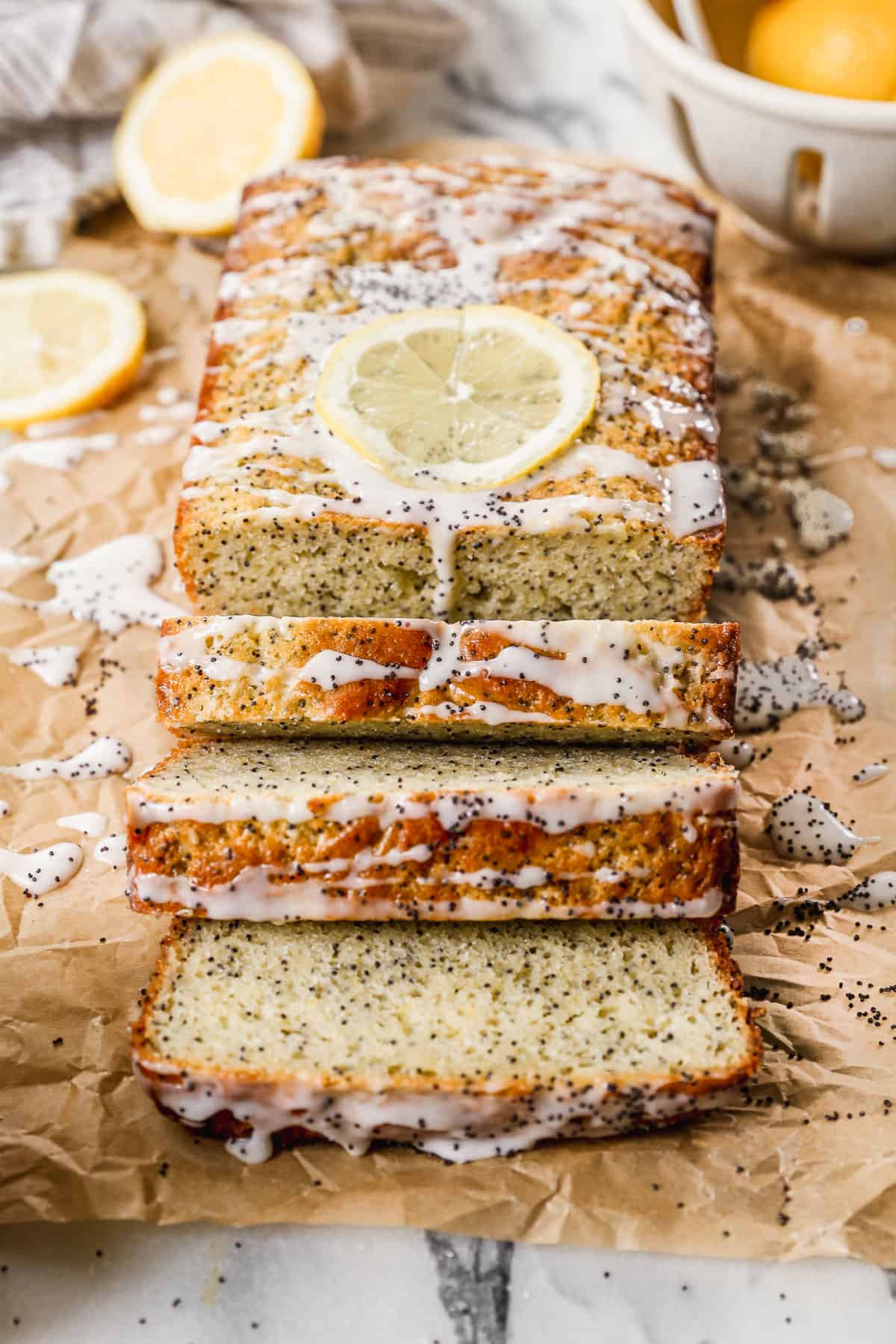 Lemon Poppy Seed Bread sliced on parchment paper and garnished with a sweet lemon glaze and a dried lemon