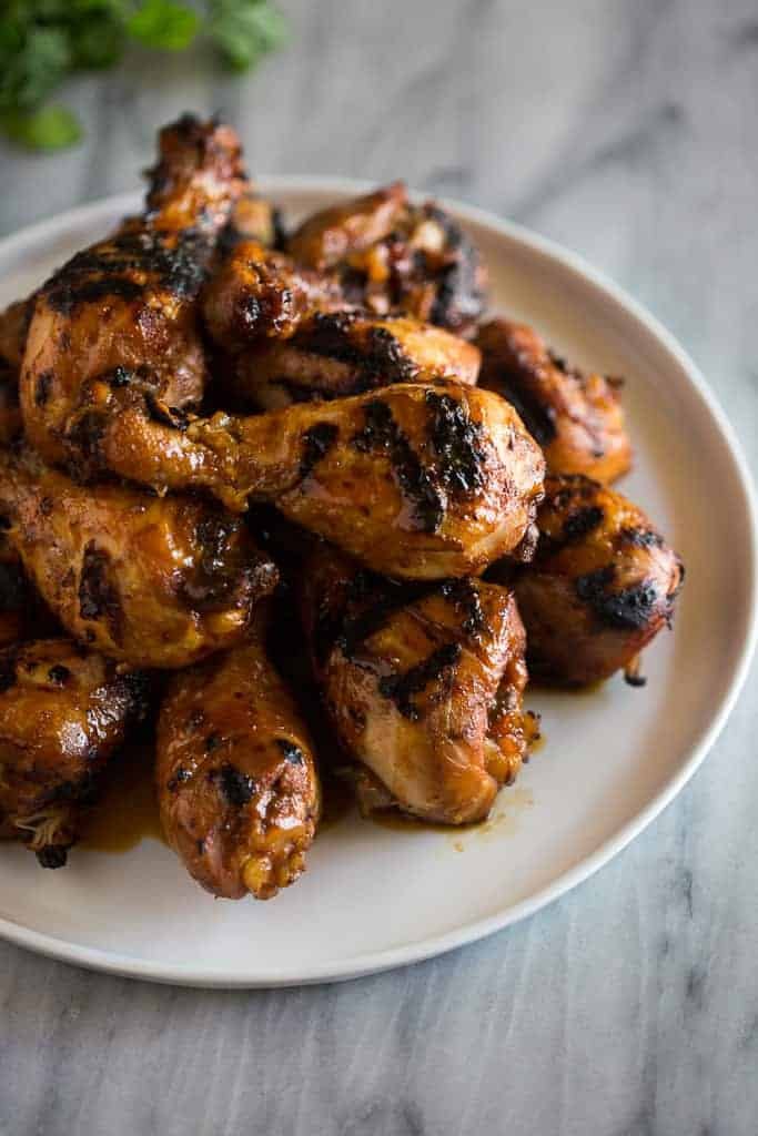 BBQ chicken drumsticks piled on a white plate