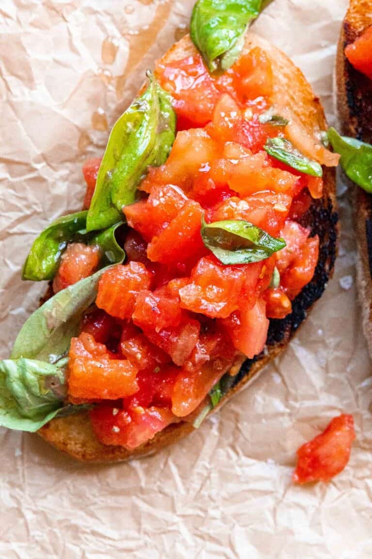 Tomato and Basil Bruschetta is made with bread, garlic, tomato, basil, and extra virgin olive oil and pictured here on crumpled wax paper. 