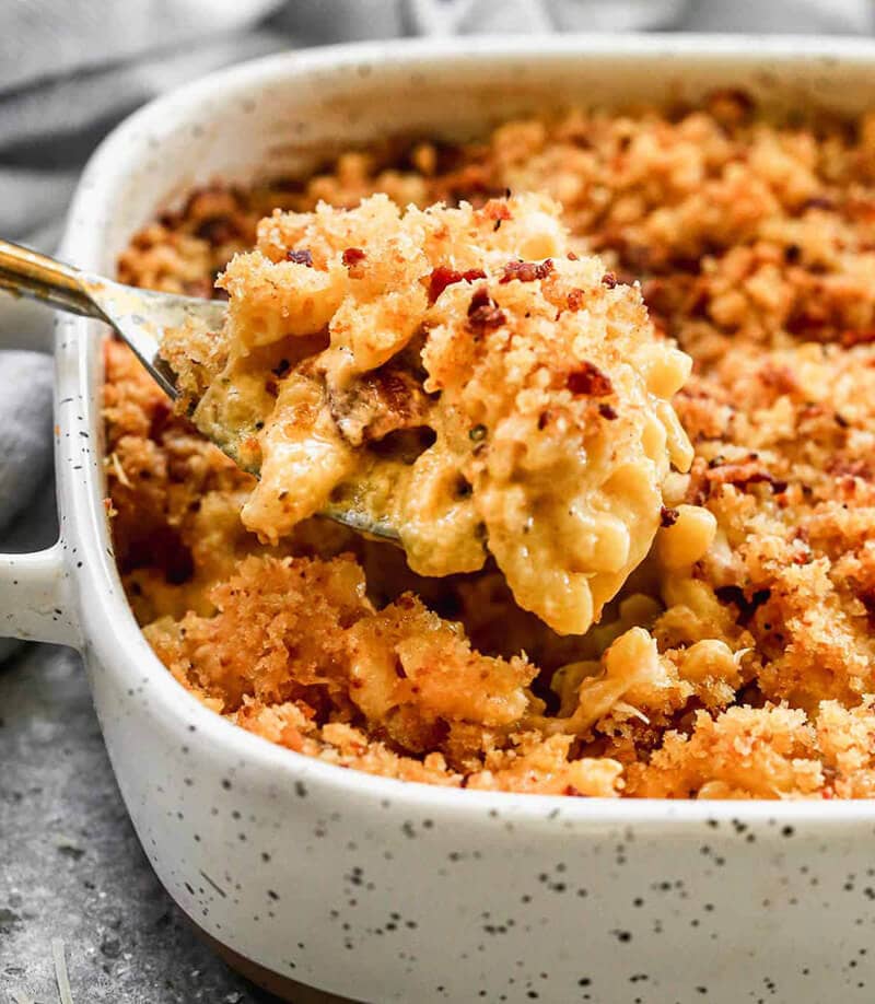 Baked Mac and Cheese showed being served with a spoon and in a white speckeled rectangle serving dish.