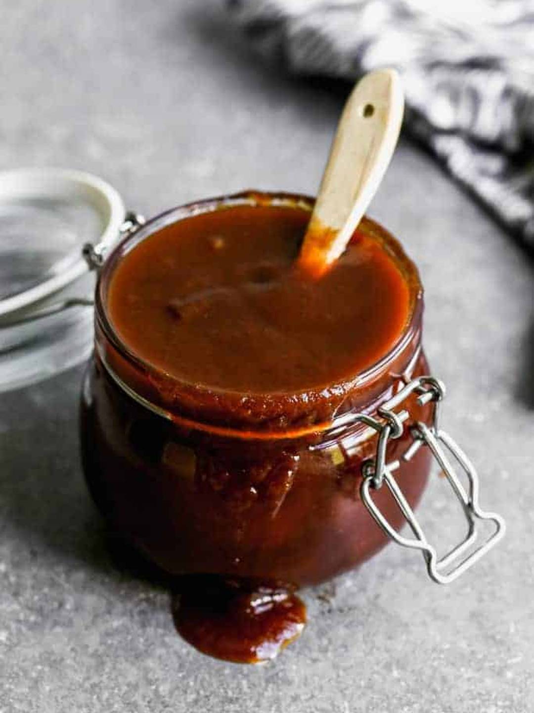 Homemade BBQ Sauce in a glass jar overflowing with a wooden spoon inside.