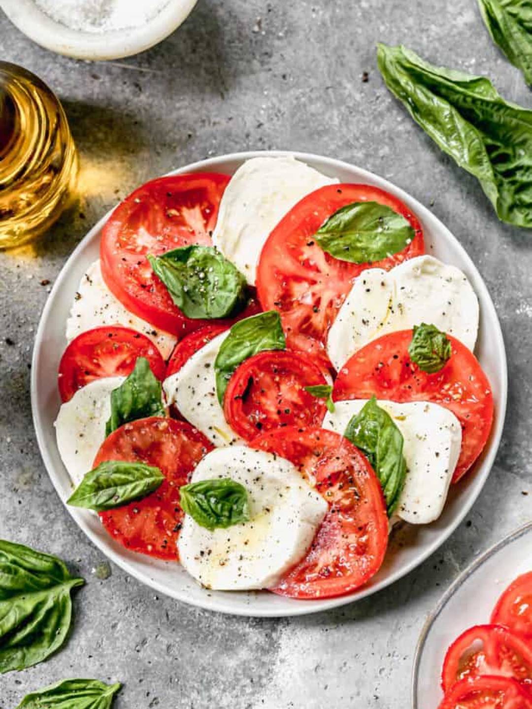Caprese Salad surrounded by ingredients arranged on a white plate. 