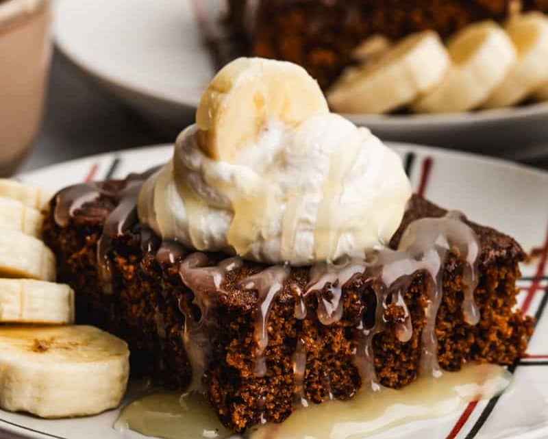 A piece of moist Gingerbread Cake, topped with whipped cream, bananas, and a homemade vanilla cream sauce.