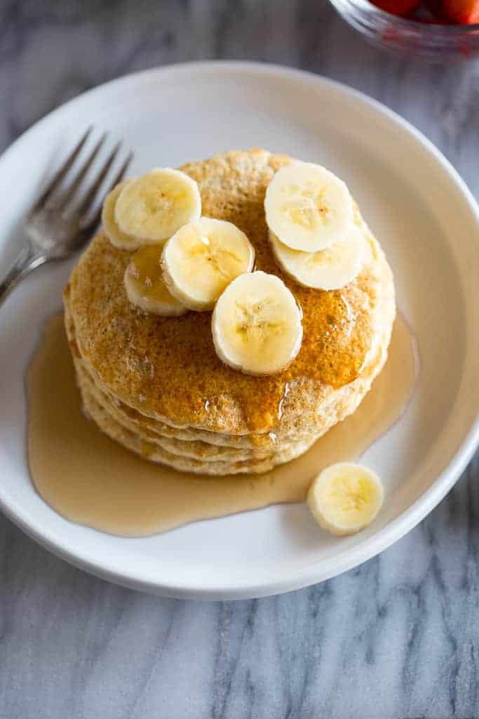 Protein pancakes stacked on a white plate and garnished with bananas and homemade syrup