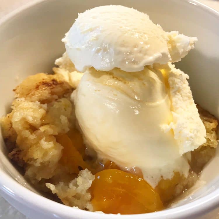 A golden bubbly peach cobbler fresh from the oven with sweet juicy peaches and a crisp buttery topping. Served warm with a scoop of vanilla ice cream.