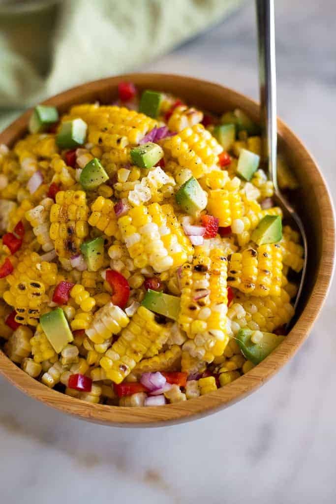 Corn salad tossed with onion, bell pepper, avocado, and served in a wood bowl