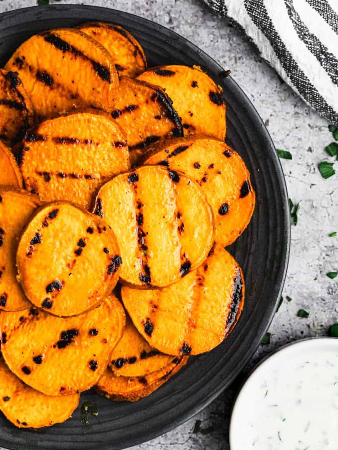 Grilled sweet potatoes served on a black plate with a black and white towel in the background.