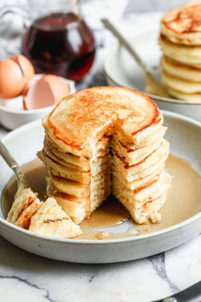 Buttermilk pancakes stacked on a white plate with homemade syrup