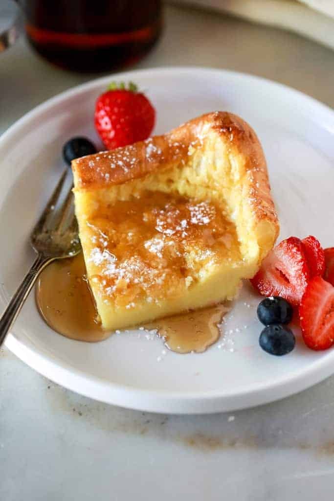 German pancakes garnished with strawberries and syrup and dusted with powdered sugarr